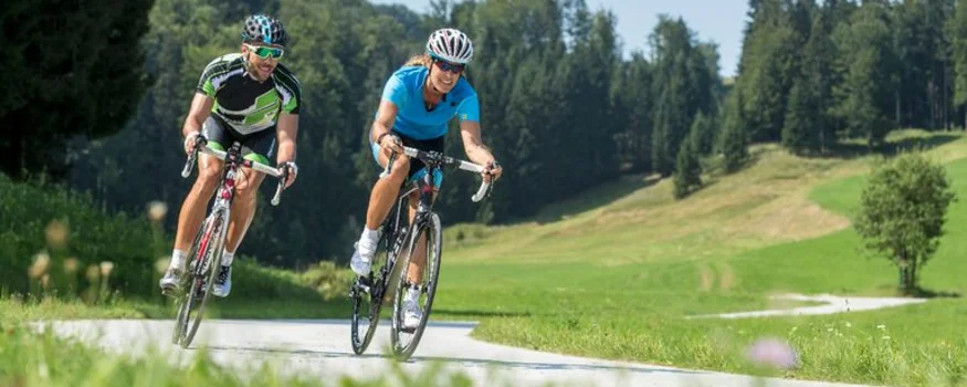 Zwei Radfahrer fahren auf Landstraße in grüner Landschaft bei Sonnenschein
