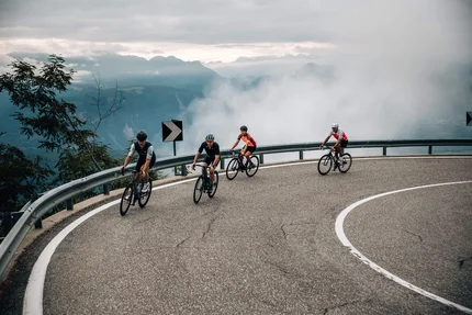 Vier Radfahrer fahren auf kurviger Bergstraße bei Nebel