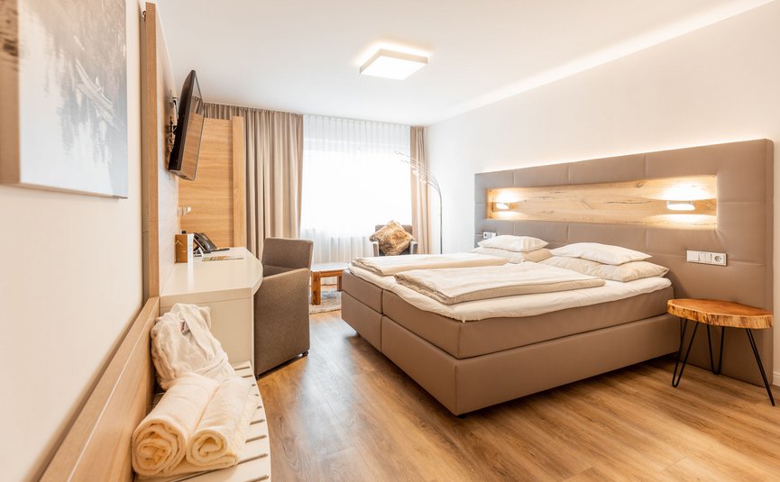 Modern hotel room with double bed, desk, and large window with curtains