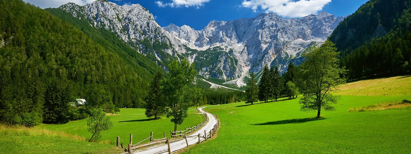 Sentiero tra prati verdi verso montagne rocciose sotto cielo azzurro
