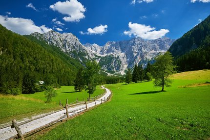 Sentiero tra prati verdi verso montagne rocciose sotto cielo azzurro