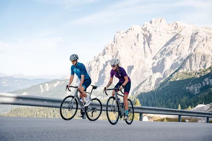 Due ciclisti pedalano su strada di montagna con montagne rocciose