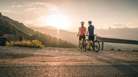 Warum Alta Badia auf jede Roadbike-Bucket-List gehört © Molography Zwei Radfahrer blicken bei Sonnenuntergang auf Berge