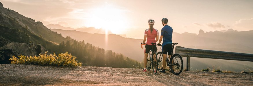 Due ciclisti guardano il tramonto sulle montagne