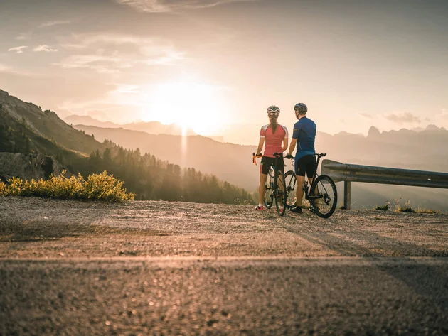 Warum Alta Badia auf jede Roadbike-Bucket-List gehört © Molography Zwei Radfahrer blicken bei Sonnenuntergang auf Berge
