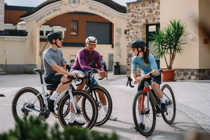 Drei Radfahrer in Sportkleidung sitzen auf ihren Fahrrädern und unterhalten sich