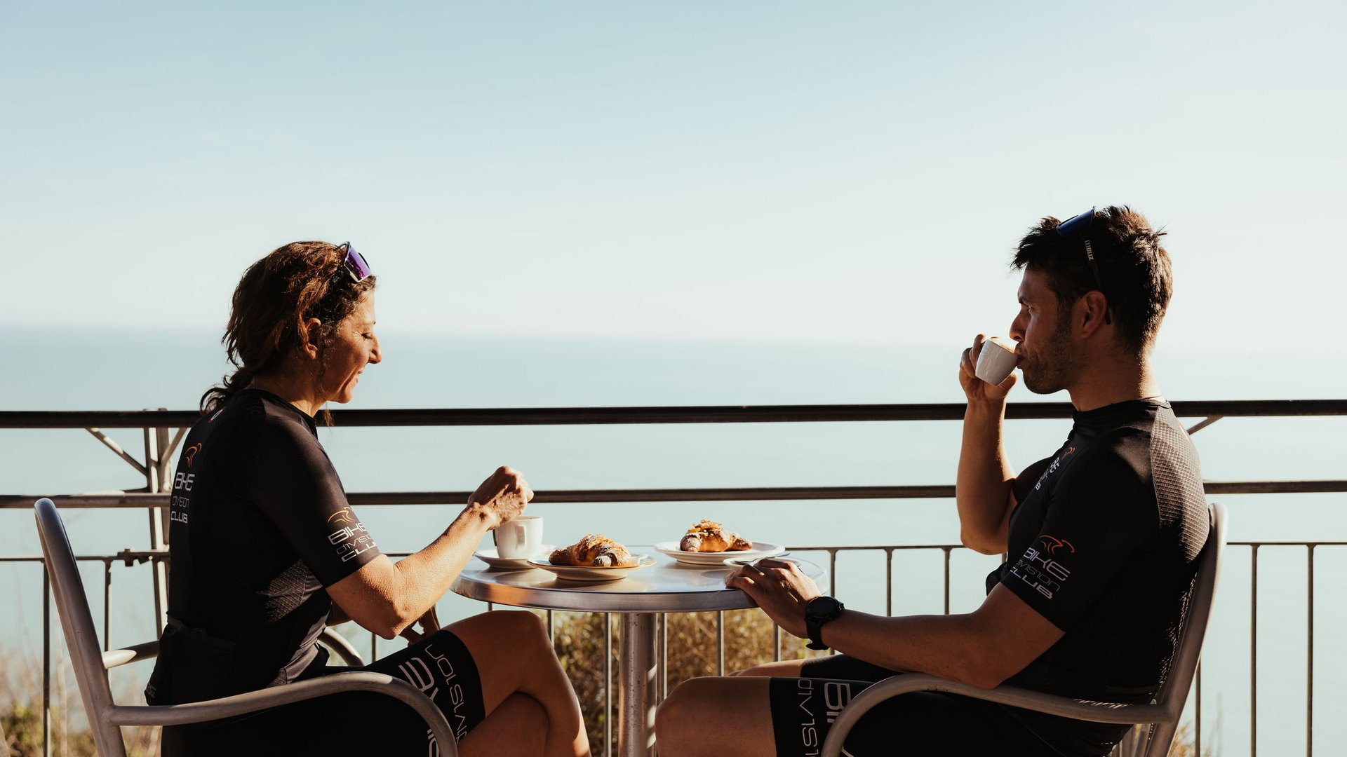 Zwei Radfahrer genießen Kaffee und Croissants auf Balkon mit Meerblick