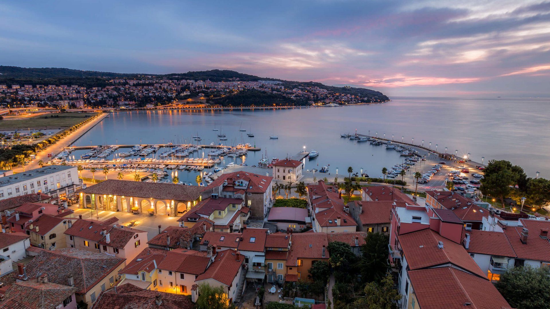 Abendlicher Blick auf Hafen und Stadt mit beleuchteten Gebäuden und Booten
