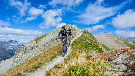 Zwei Mountainbiker fahren auf schmalem Gebirgspfad bei klarem Himmel