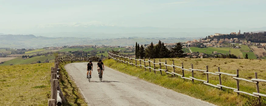 Zwei Radfahrer unterwegs auf Landstraße mit ländlicher Landschaft im Hintergrund