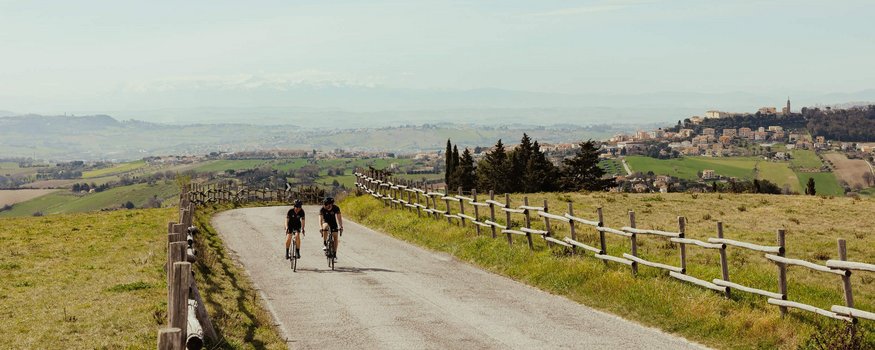 Zwei Radfahrer unterwegs auf Landstraße mit ländlicher Landschaft im Hintergrund