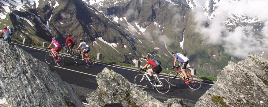 Sportcamp Woferlgut **** © Sportcamp Woferlgut Bruck Radfahrer fahren auf Bergstraße mit schneebedeckten Alpen im Hintergrund