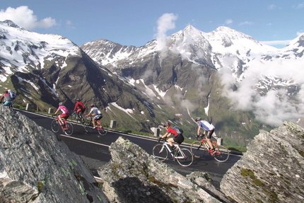 Ciclisti in salita su strada di montagna con Alpi innevate sullo sfondo