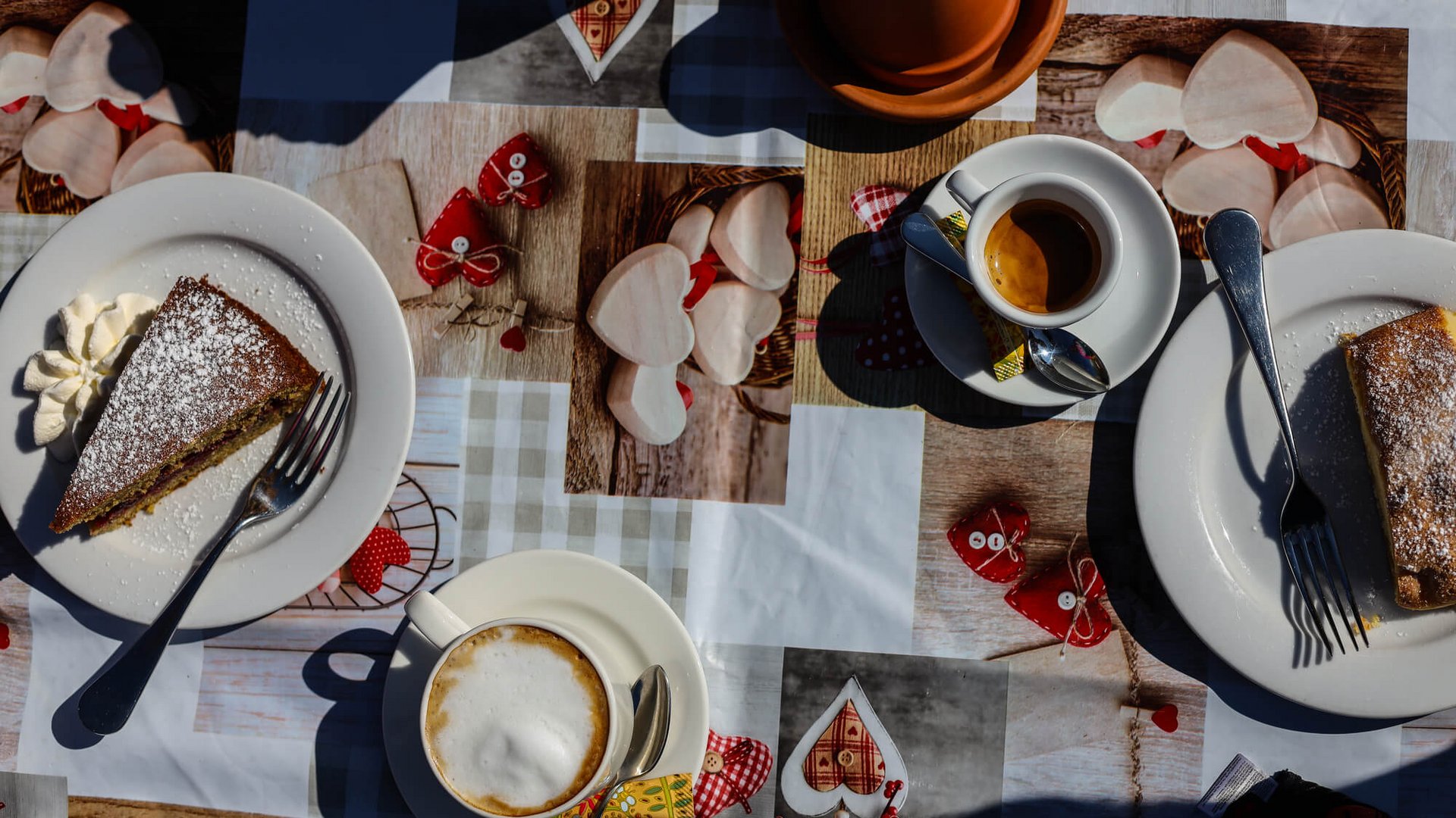 Tisch mit zwei Kuchenstücken, Cappuccino und Espresso auf dekorativem Tischtuch