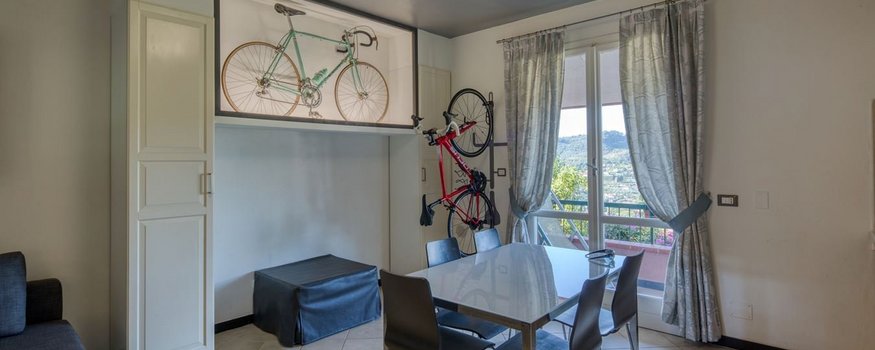 Zona pranzo con tavolo, sedie, balcone e biciclette appese al muro