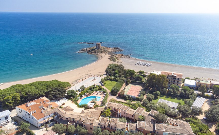 Aerial view of beach with blue sea, pool, and buildings in the foreground