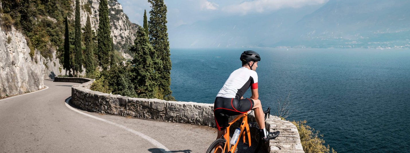 Radfahrer auf kurviger Straße mit Blick auf See und Berge