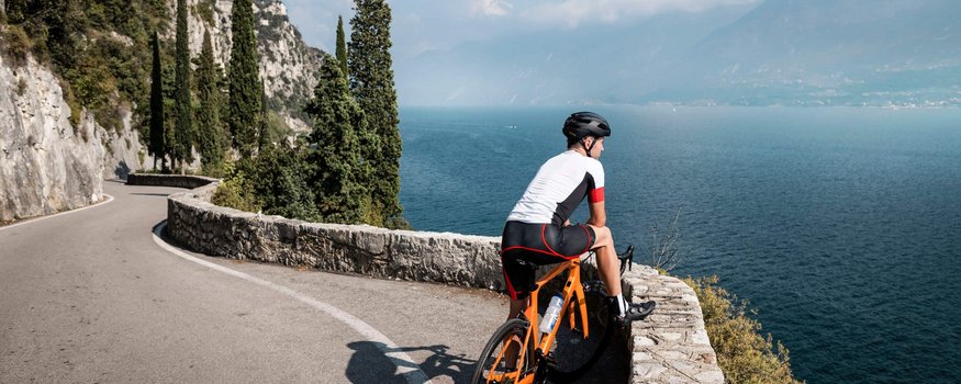 Radfahrer auf kurviger Straße mit Blick auf See und Berge