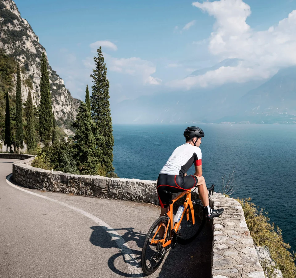 Zwischen Passstraßen, See & Dolce Vita beim Rennradurlaub am nördlichen Gardasee © Alex Moling Radfahrer auf kurviger Straße mit Blick auf See und Berge