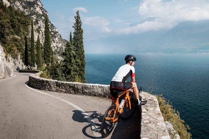 Ciclista su strada tortuosa con vista su lago e montagne