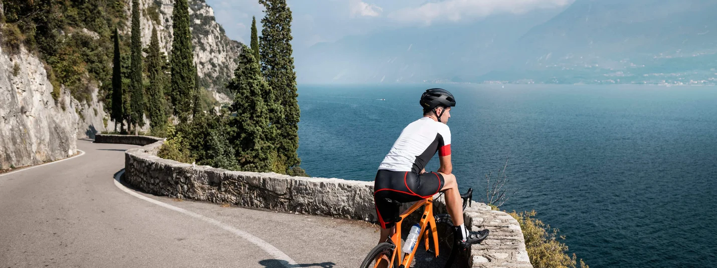 Tour del Lago di Garda © Alex Moling Ciclista su strada tortuosa con vista su lago e montagne