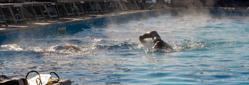 Two swimmers in a heated outdoor pool early morning