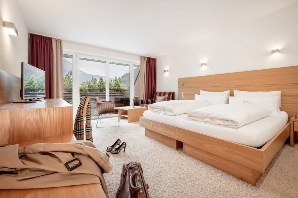 Helles Hotelzimmer mit Doppelbett, TV und Balkon mit Bergblick