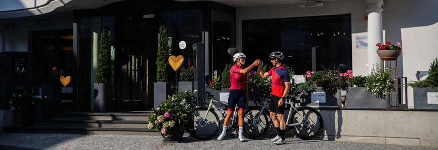Two cyclists fist bump in front of Central Hotel