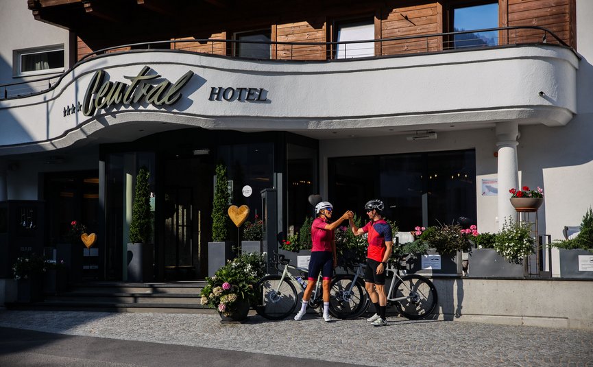 Two cyclists fist bump in front of Central Hotel