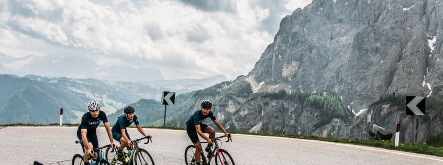 Roadbike Week Drie wielrenners op bergweg met rotsen en bewolkte lucht