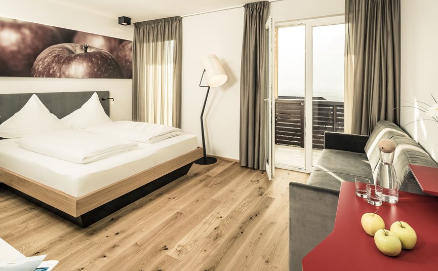 Camera d'hotel moderna con letto, divano, balcone e quadro di mele