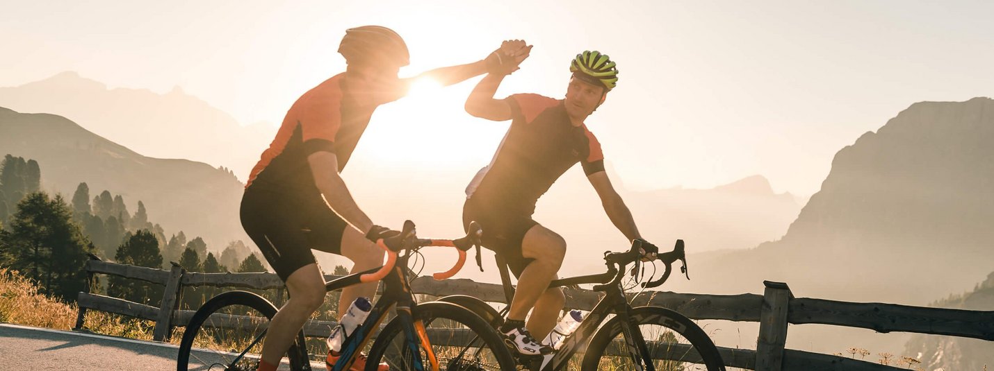 Zwei Rennradfahrer geben sich beim Sonnenuntergang High Five auf einer Bergstraße