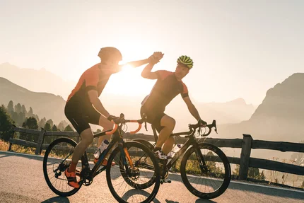Twee wielrenners geven elkaar een high five op een bergweg bij zonsondergang