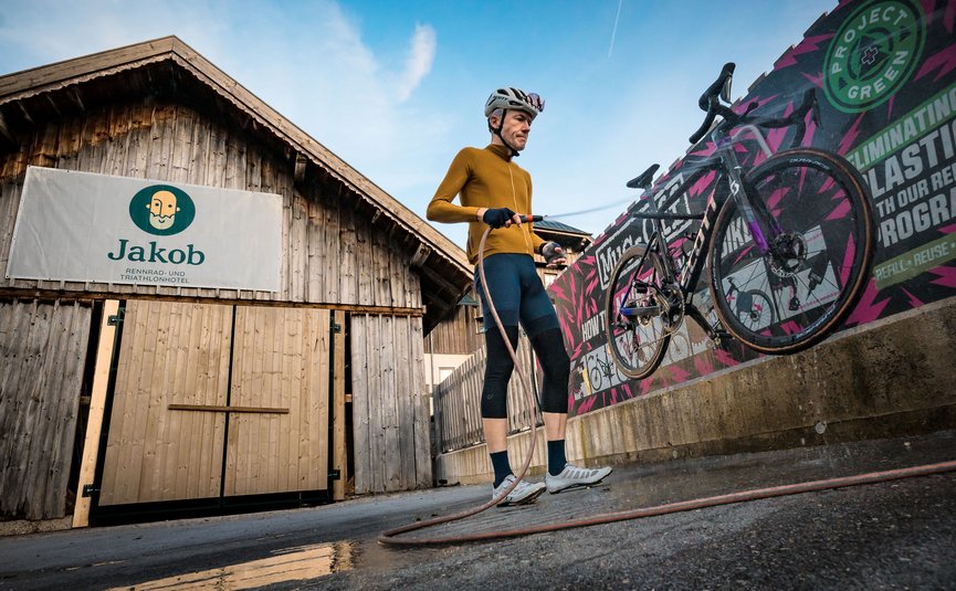 Cyclist cleaning road bike with hose in front of wooden building