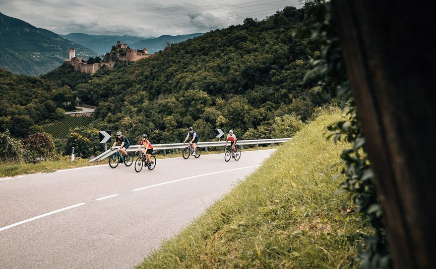 Quattro ciclisti su strada di montagna tortuosa con colline boschive e castello