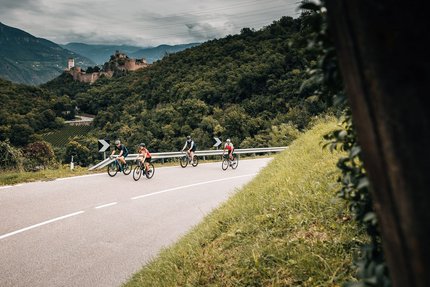 Quattro ciclisti su strada di montagna tortuosa con colline boschive e castello