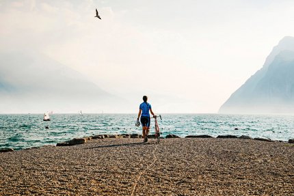 Ciclista al lago con montagne e barche a vela sullo sfondo