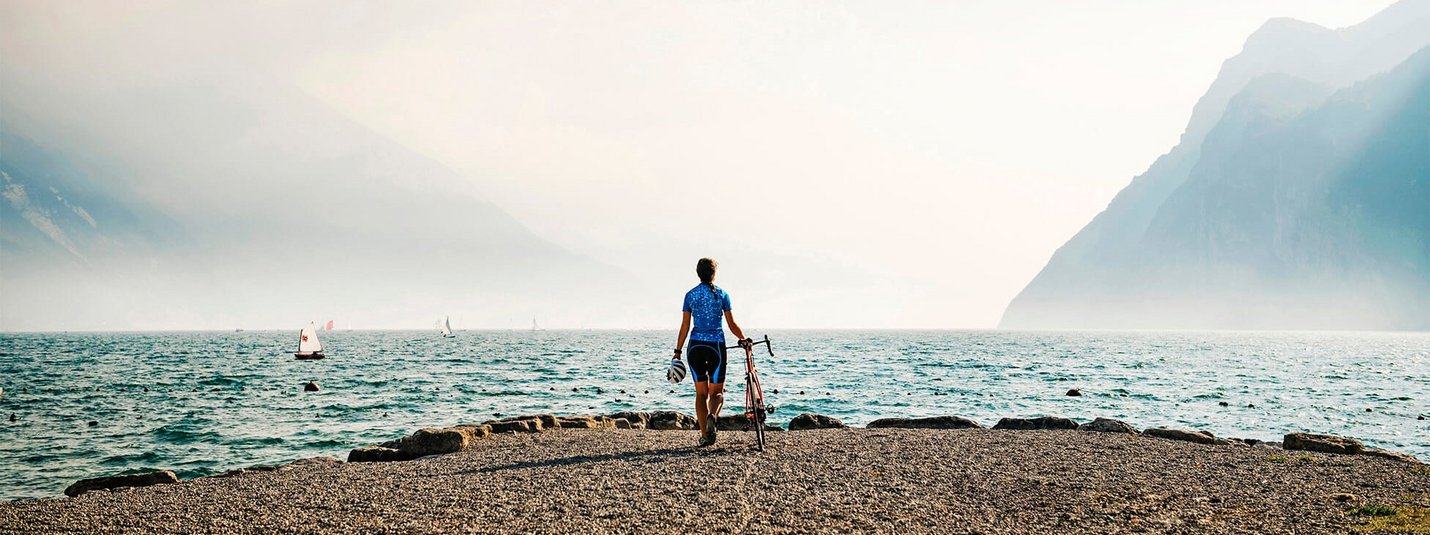 Fietser aan het meer met bergen en zeilboten op de achtergrond