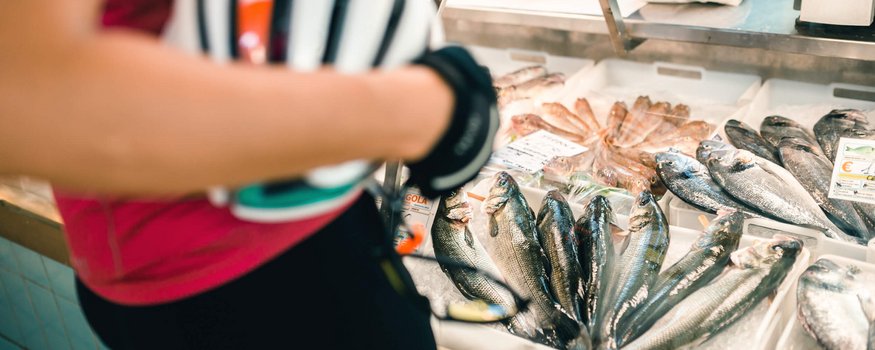 Person hält Fahrradhelm vor Fischtheke mit frischen Fischen im Markt
