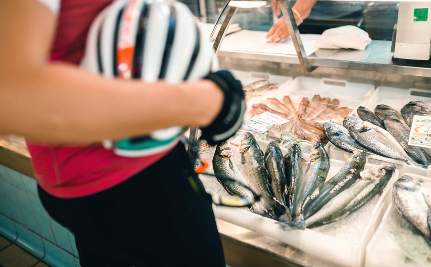Person holding bicycle helmet in front of fresh fish display at market