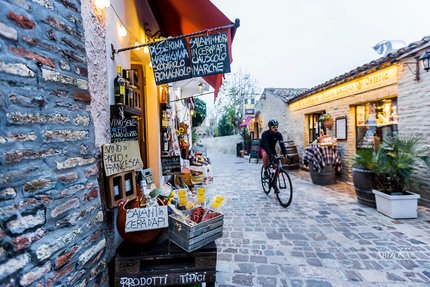 Cyclist rides through narrow alley with Italian deli shop