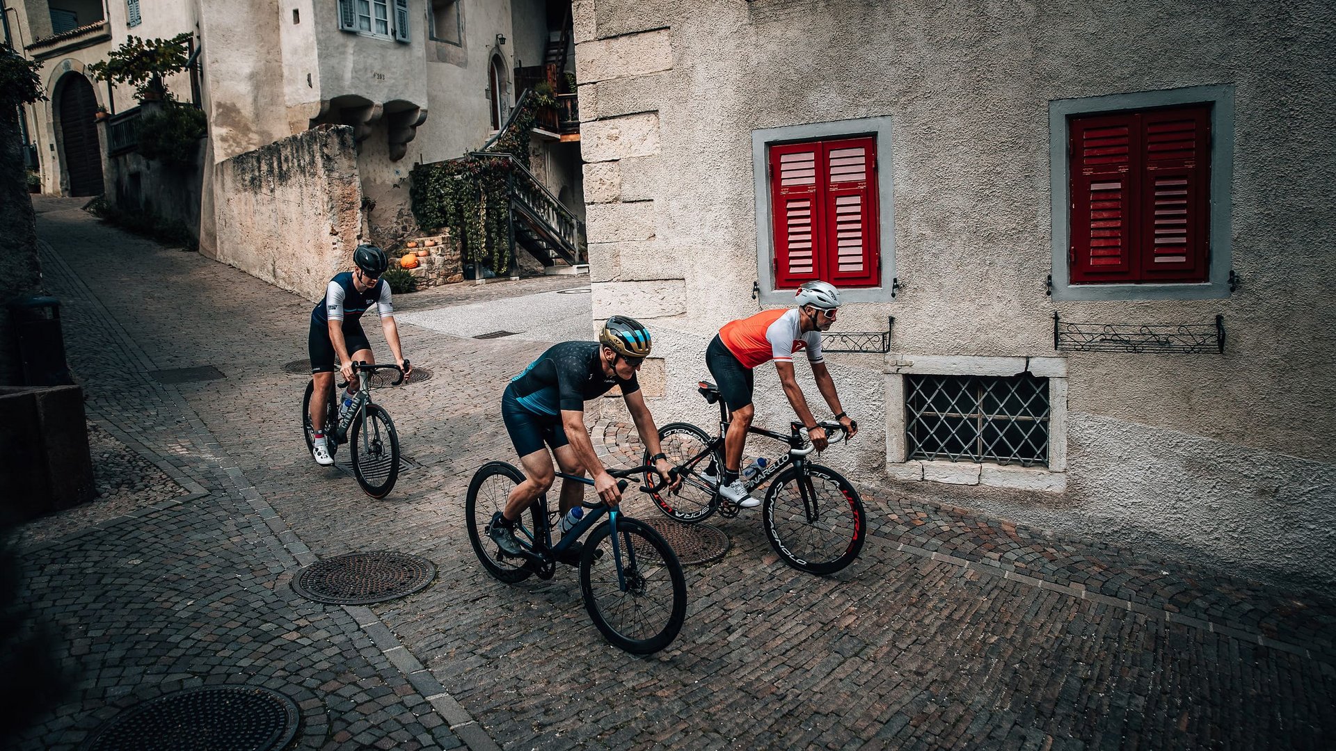 Drei Radfahrer fahren durch gepflasterte Straßen in einem alten Dorf.