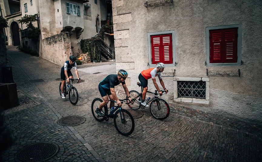Drei Radfahrer fahren durch gepflasterte Straßen in einem alten Dorf.