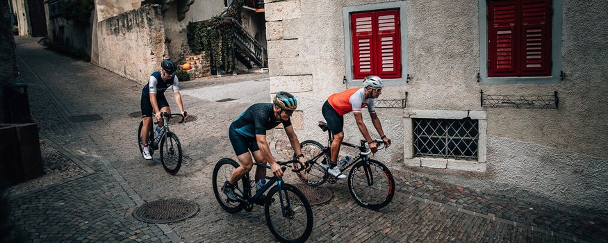 Drei Radfahrer fahren durch gepflasterte Straßen in einem alten Dorf.