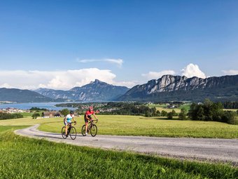 Zwei Radfahrer fahren auf Landstraße mit Bergen und See im Hintergrund