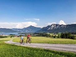 Due ciclisti su strada di campagna con montagne e lago sullo sfondo