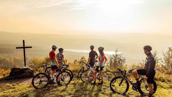 Fünf Radfahrer mit Rennrädern stehen bei Sonnenuntergang auf einem Hügel