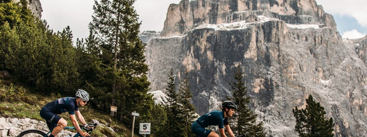 Zwei Rennradfahrer fahren eine Bergstraße mit Felsen im Hintergrund hinauf