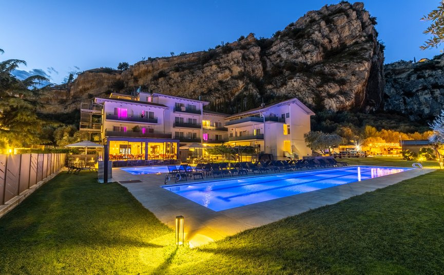 Beleuchtetes Hotel mit Außenpool vor Felsen bei Abenddämmerung