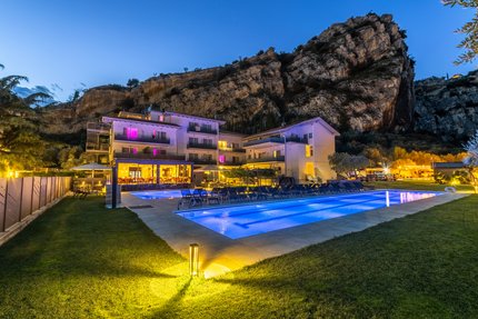 Lit hotel with outdoor pool in front of cliffs at dusk